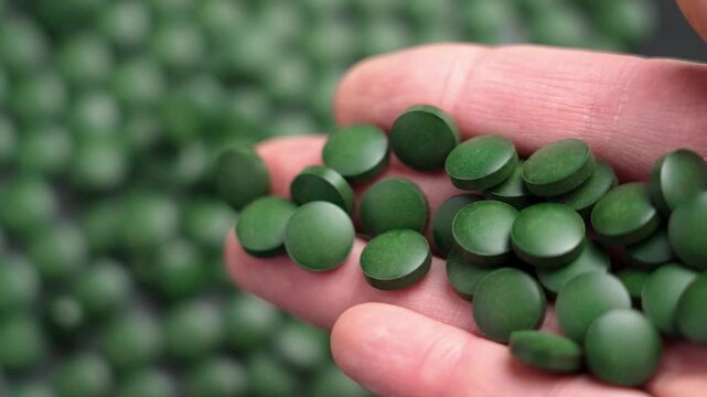 Close-up view of falling spirulina pills from hand. Deep green color and round shape. Ideal for natural health enthusiasts. Promotes energy and supports immunity. Slow motion