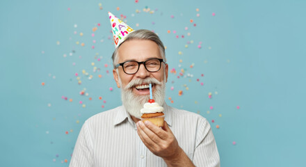 Joyful senior man celebrating birthday with cupcake and party hat against colorful confetti background