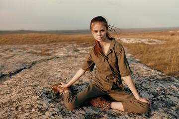 Peaceful young woman sitting on rock in middle of field with legs crossed surrounded by nature and beauty