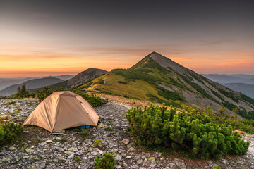 Tent Camping In The Mountains, First Morning Light. Campsite with a dome tent on a high mountain bluff at sunrise.Travel concept and background.