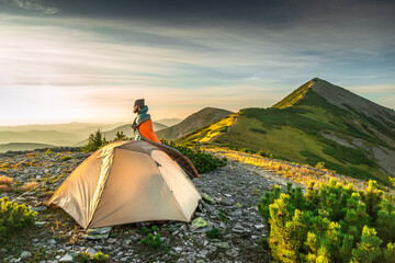 Stylish bearded man wrapped in a sleeping bag watches sunrise outside camping tent. Weekend...
