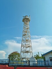 Cirebon, Indonesia - Nov 02, 2024: White lighthouse made of steel with greenery trees and grey sky as the background