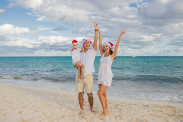 Happy family celebrates Christmas on the beach. Mom, dad and son in holiday hats on the beach celebrate the New Year