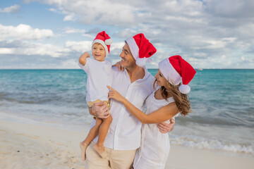 Happy family celebrates Christmas on the beach. Mom, dad and son in holiday hats on the beach celebrate the New Year