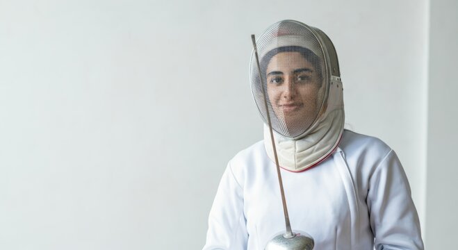 Female fencer in protective gear holding epee against neutral background - Powered by Adobe