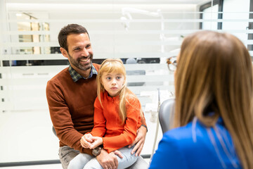 A father and his daughter sit in a dental clinic during a consultation, emphasizing family care and...