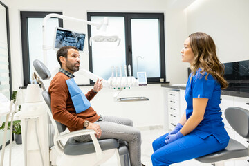 A patient converses with a dentist in a modern clinic, seated comfortably, with dental tools and...