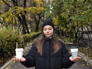 SeriousGirl holding takeaway coffee cup and a disposable paper cup with plastic lid. Conscious...