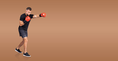 A focused man boxer in training throws a punch while wearing red boxing gloves. He is dressed in casual athletic wear, showcasing his dedication and skill in a well-lit indoor setting.