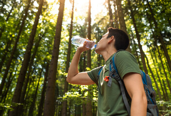 Active man drinking bottle of water while hiking through the forest 