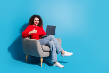 Full length photo of lovely young lady sit armchair netbook thumb up dressed stylish red garment isolated on blue color background