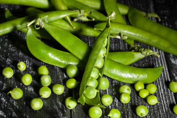 open green peas on black wood background