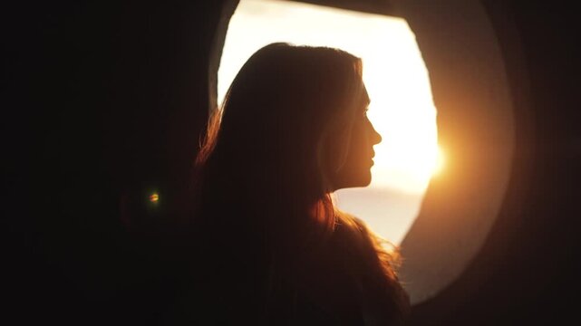 Atmospheric, cinematic video of a girl looking into the golden sunset near a round window, sun rays, beauty, love, calm, melancholy, pleasure, face portrait, life, moment, alive, feelings, deep