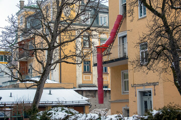 Salzburg, Austria - 01.13.2024: Hanging sections of a red construction waste chute on the facade of...