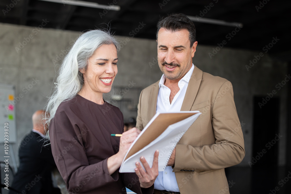 Poster a woman and a man engage in a collaborative discussion in a modern office. the woman writes on a not