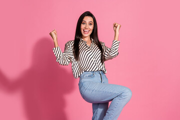 Young woman rejoicing with enthusiasm against a vibrant pink background in a stylish casual outfit