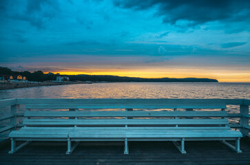 White bench on a wooden pier inviting visitors to enjoy the beautiful sunset over the baltic sea in...