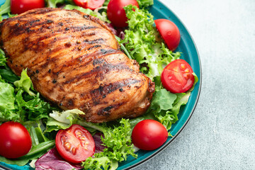 Grilled chicken breast ( fillet ) with lattuce salad and cherry tomatoes . Top view