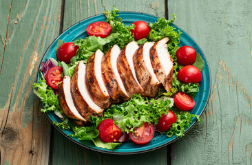 Grilled chicken breast ( fillet ) with lattuce salad and cherry tomatoes . Top view