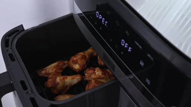 Opening air fryer with chicken drumsticks inside, close-up view of roasted meat. Zoom