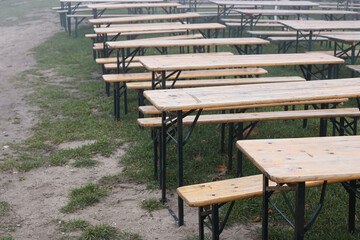 Fototapeta premium Empty wooden picnic table and bench in a foggy park setting. Abandoned outdoor seating on a rainy, overcast day, with mist hanging in the air. Scene of a canceled gathering due to poor weather.
