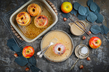 Traditional oven baked apples with crushed nuts, cinnamon and butter served with homemade vanilla sauce as top view in a design plate