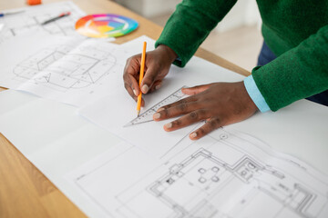 A person is focused on designing architectural plans using a ruler and pencil on a wooden table....