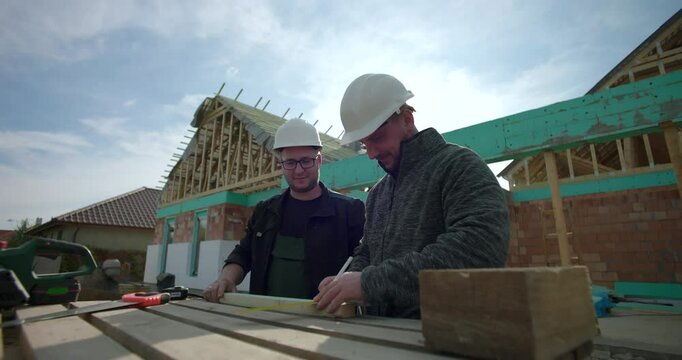 Close-up of builders working together on a new house project, measuring and marking wooden planks, teamwork and collaboration, hard hats, tools, construction in progress