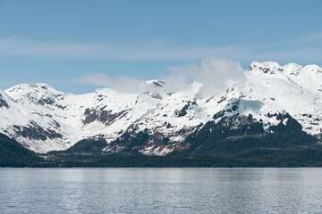 Fototapeta premium Sun and shadows on a snow covered mountain with clouds and mist, Alaska, USA