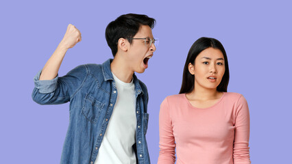 Domestic violence. Young asian man threatening his woman with his fist, gray studio background