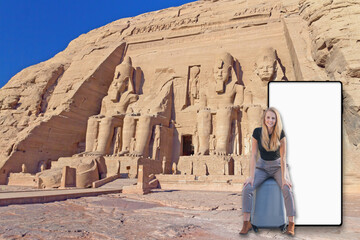 Girl sitting on suitcase in front of Abu Simbel Temple in Egypt. Blank mobile screen is ready for...