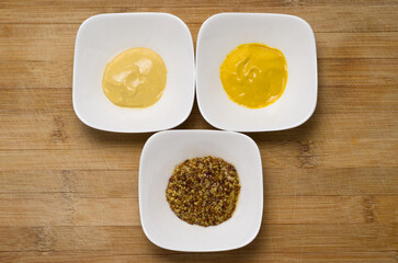 Top View of Various Types of Mustard in White Bowls on Wood Cutting Board