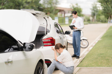 Distressed Woman After Car Accident: A woman sits on the ground beside her damaged car, looking...