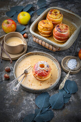 Traditional oven baked apples with crushed nuts, cinnamon and butter served with homemade vanilla sauce as close-up in a design plate