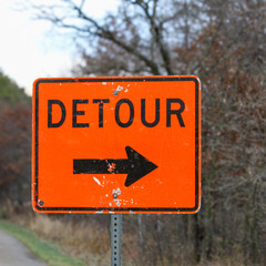 close-up of orange detour sign surrounded by autumn trees in the background