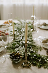 Vertical high angle shot of white long candles in beautiful silver candle holder on table pine garland and crystal champagne glasses and plates