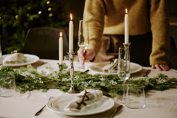 Unrecognizable woman serving X-mas table with crystal champagne glasses, table covered with snow white cotton tablecloth and polished plates with napkins