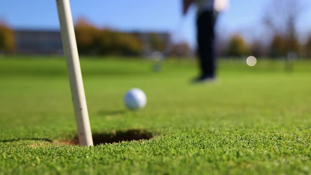 Close-up of golf ball sinking into hole with senior golfer in background