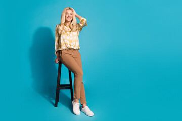 Full length photo of stunning mature lady sit chair touch head dressed stylish formalwear clothes isolated on cyan color background