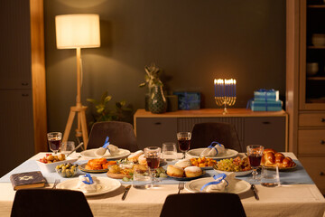 Served table with pastries, appetizers and alcohol in center of cozy dining room prepared for Hanukkah celebration