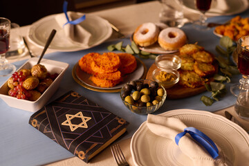 Medium close up of Torah with star of David on cover surrounded with appetizers and traditional Jewish treat for Hanukkah holiday