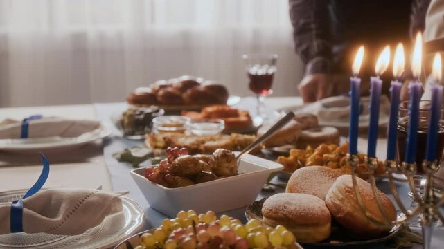 Close up view of hands of family members serving traditional Jewish dishes on festive table decorated with lit menorah candles while preparing to celebrate Hanukkah at home