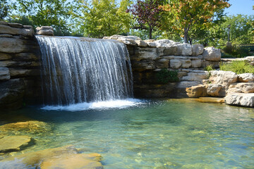Naklejka premium The waterfall flows gracefully into a clear pond, creating a peaceful natural retreat