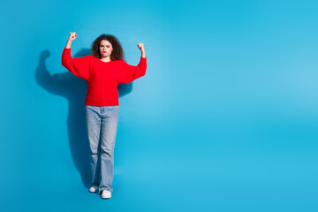 Full body photo of attractive young woman flexing show muscles dressed stylish red clothes isolated on blue color background