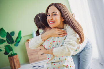 Naklejka premium Joyful young mother hugging her little daughter at home, enjoying a relaxing spring day in the living room, creating memories together.