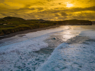 Santa Barbara beach with volcanic sand and turquoise Atlantic ocean waves in Sao Miguel, Azores. Aerial sunset view of coast in Ribeira Grande town