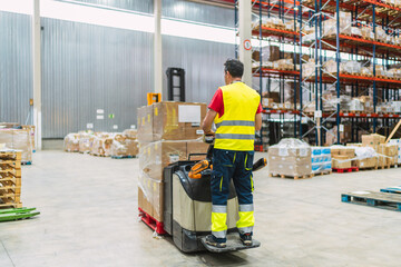 Warehouse worker moving boxes with powered pallet jack in logistics center