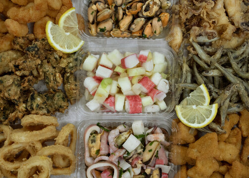 Seafood antipasti. Top view of a large box with different dishes such as fried squid rings and shrimps, fritters, squid and mussels with provencal, fish nuggets and salads