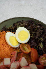 Healthy salad. Top view of a bowl with a salad made with kani kama, cucumber, carrot, cherry tomatoes, purple lettuce and a hard boiled egg