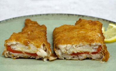 Mediterranean food. Closeup view of a sliced battered hake filet stuffed with melted mozzarella cheese and red bell pepper	
